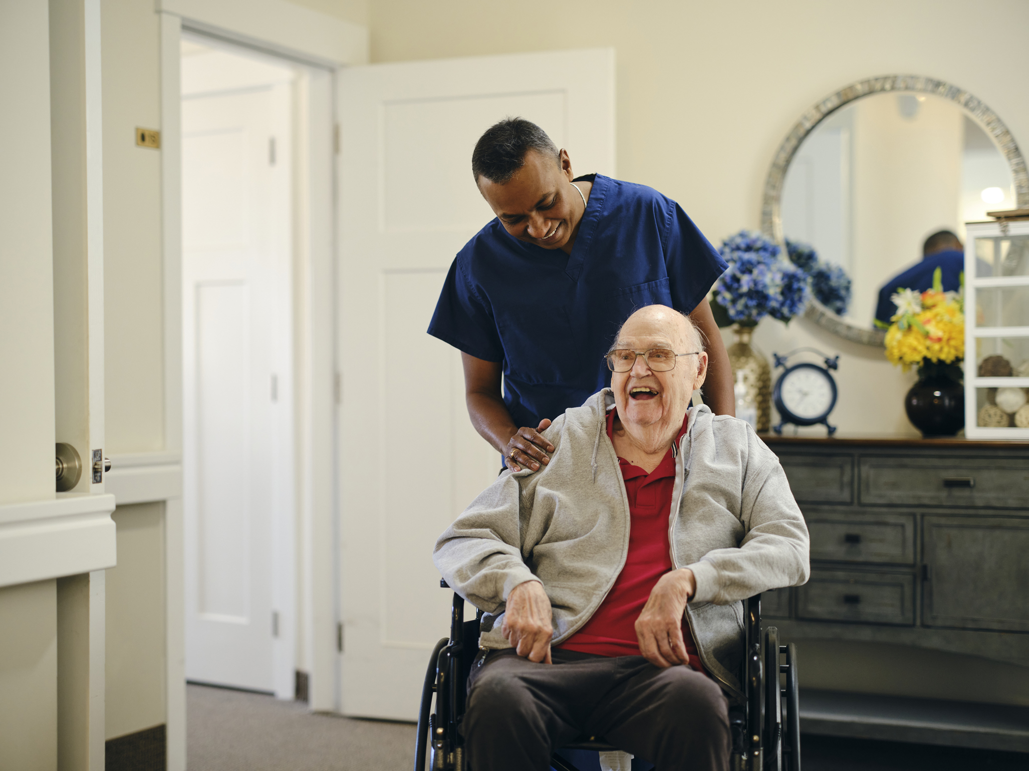 Smiling male caregiver helping an elderly man seated in a wheelchair move safely.