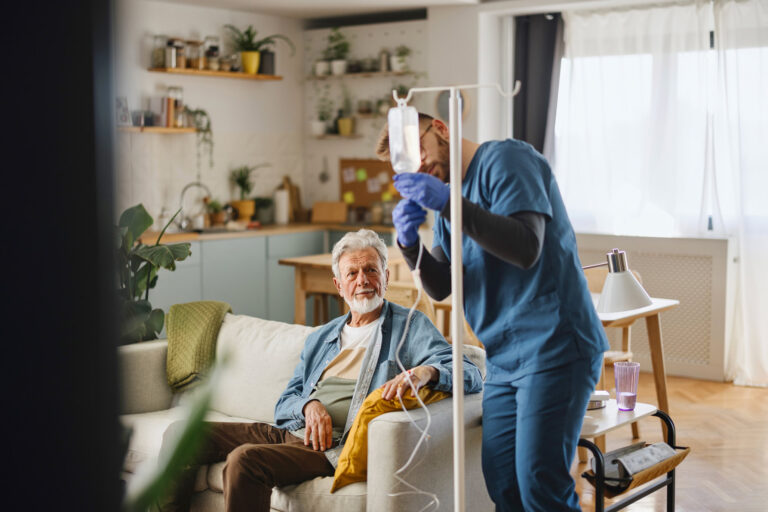 Skilled male nurse providing IV therapy for elderly man in wheelchair.